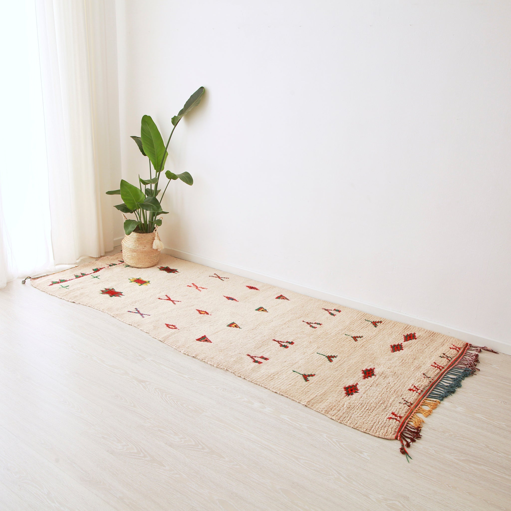 tappeto azilal vintage per corridoio su base bianca con piccoli disegni colorati che ri ripetono su 8 linee. Sul tappeto c'è una pianta