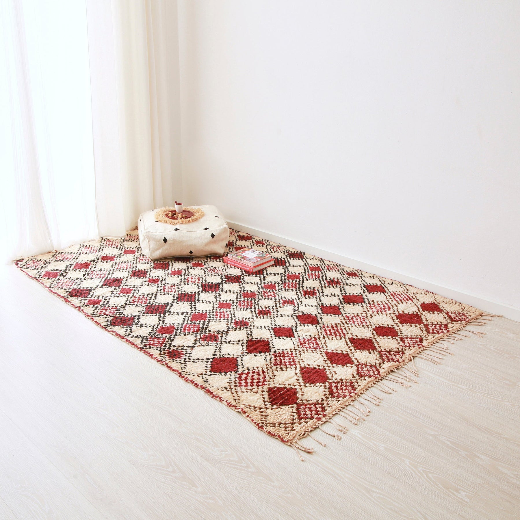 grande tappeto azilal vintage su base bianca con rombi dal bordo nero e interno di varie tonalità di rosso. Sul tappeto c'è una cesta con all'interno due cuscini in sabra rosa e azzurro