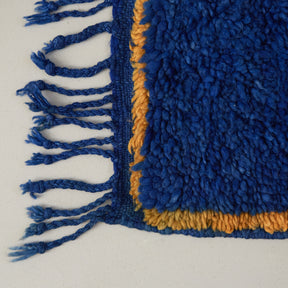 dettaglio dell'angolo e della frangia di un tappeto beni mguild blu con bordo zafferano e frangia blu