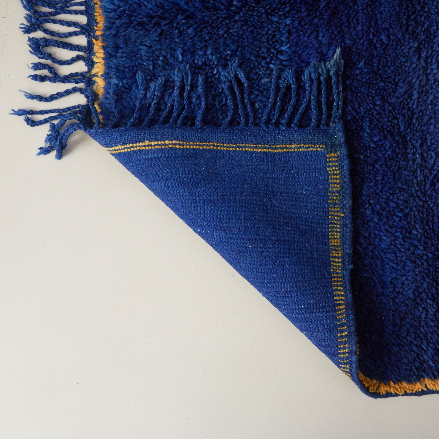 dettaglio del retro di un tappeto beni mguild blu con bordo zafferano e frangia blu