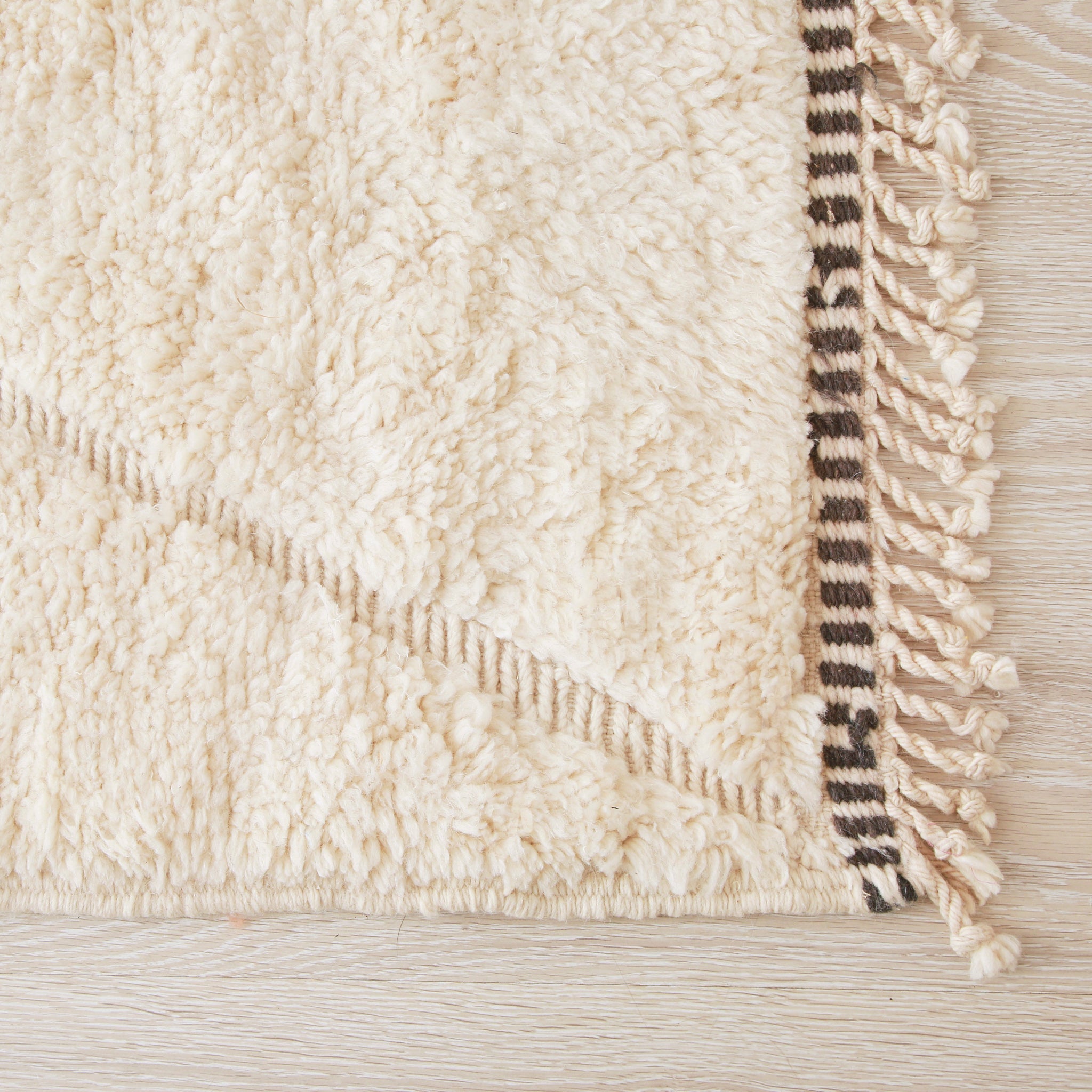 angolo di un tappeto beni mrirt in lana bianca e bordo della frangia a linee bianco e nero
