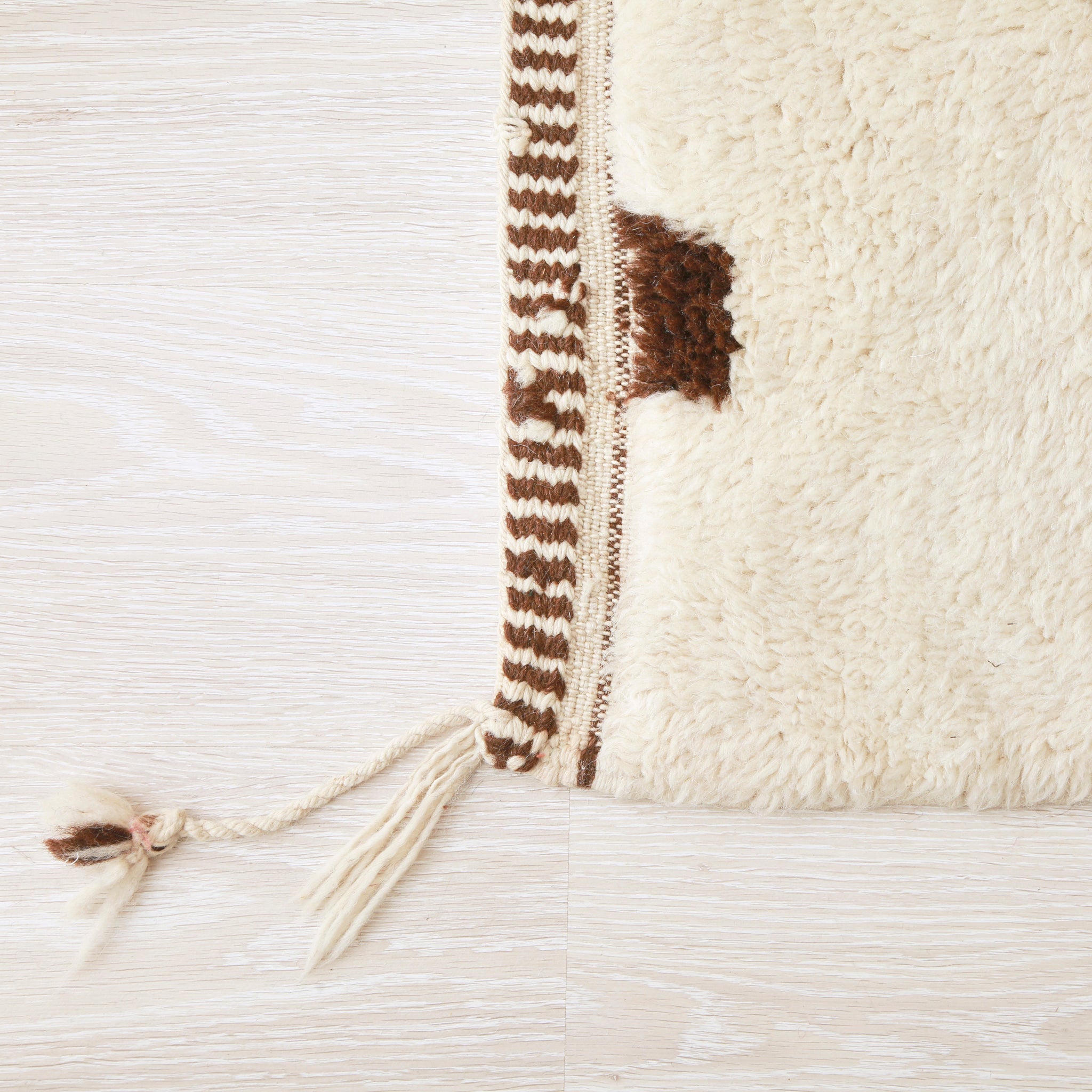 angolo di un tappeto beni mrirt bianco nel quale si nota l'alta qualità della lana non'è la precisione con la quale è stato realizzato il bordo del tappeto con bande sottili bianche e marroni