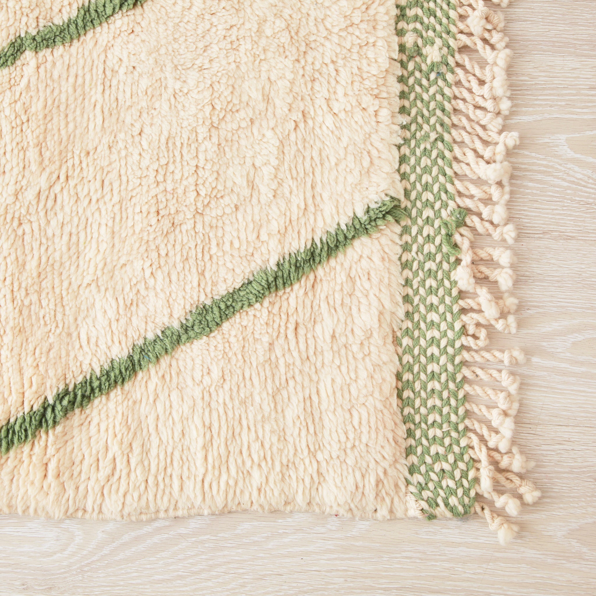 angolo di un tappeto beni mrirt in lana bianca con due riche verdi e bordo della frangia ricamato in bianco e verde