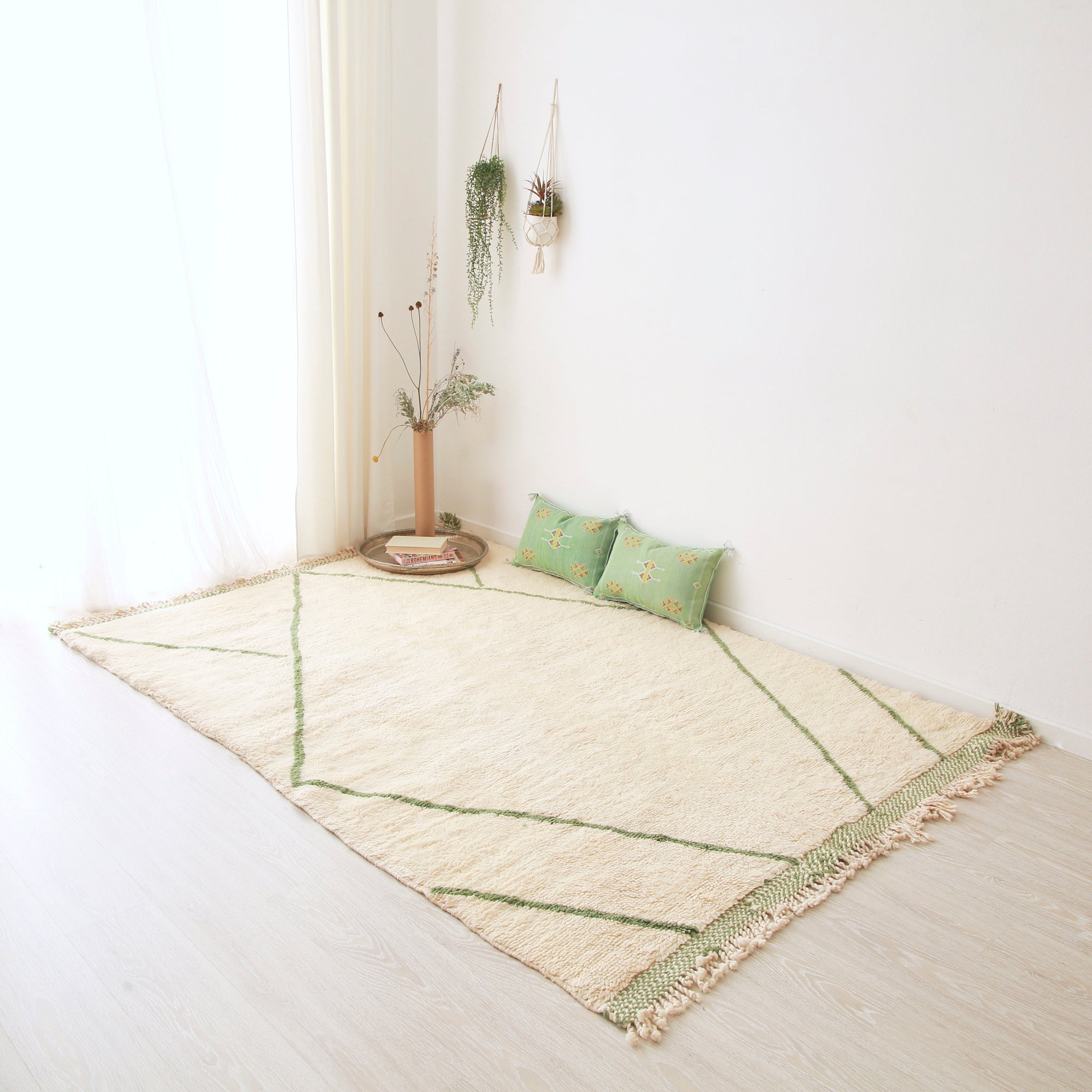 tappeto beni mrirt bianco con righe verdi appoggito sul pavimento. Sul tappeto ci sono due cuscini verdi in sabra, un piatto in argento e una composizione floreale. Sulla parete sono appese due painte