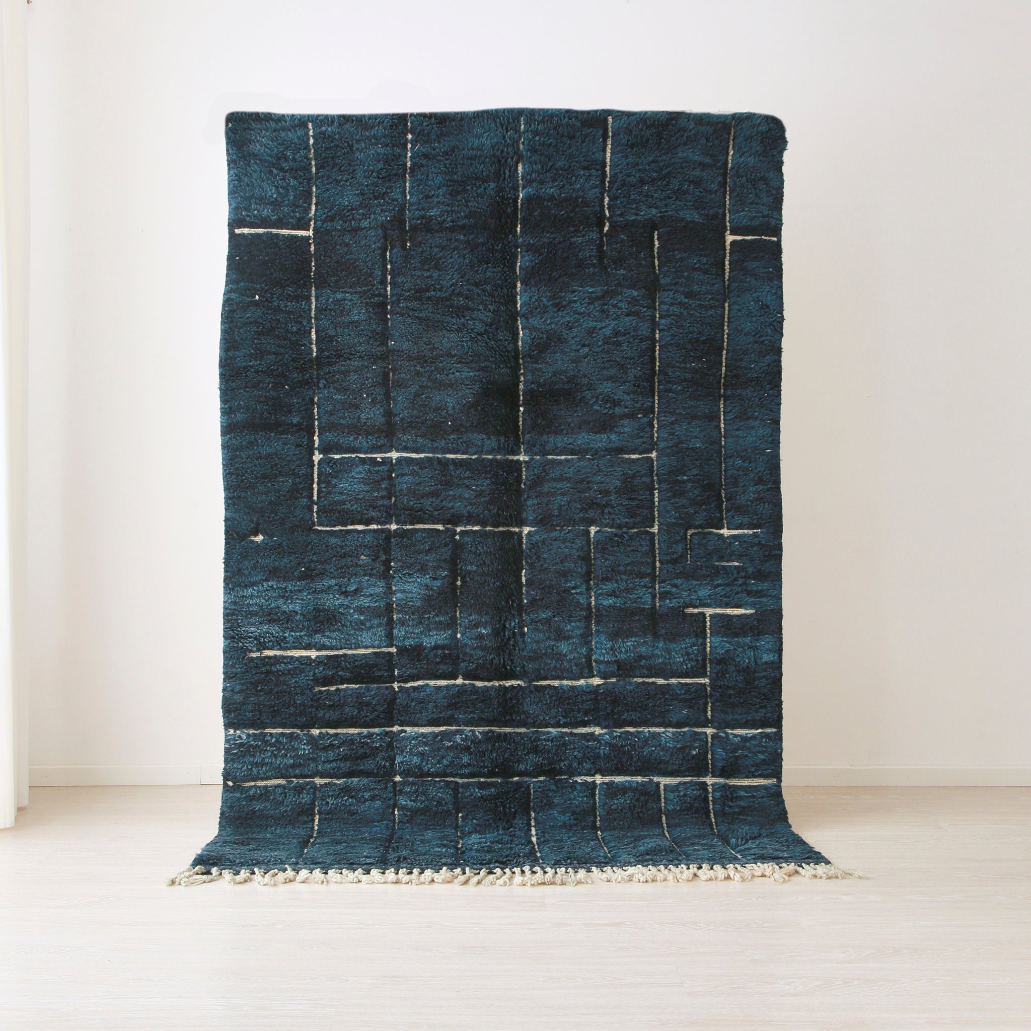 tappeto beni mrirt realizzato in lana tinta di blu. Sul tappeto emergono delle incisioni bianche che creano un disegno moderno