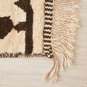 Dettaglio dell'angolo di un tappeto beni mrirt, con i bordi ricamati di marrone e bianco, gli stessi colori presti sul tappeto