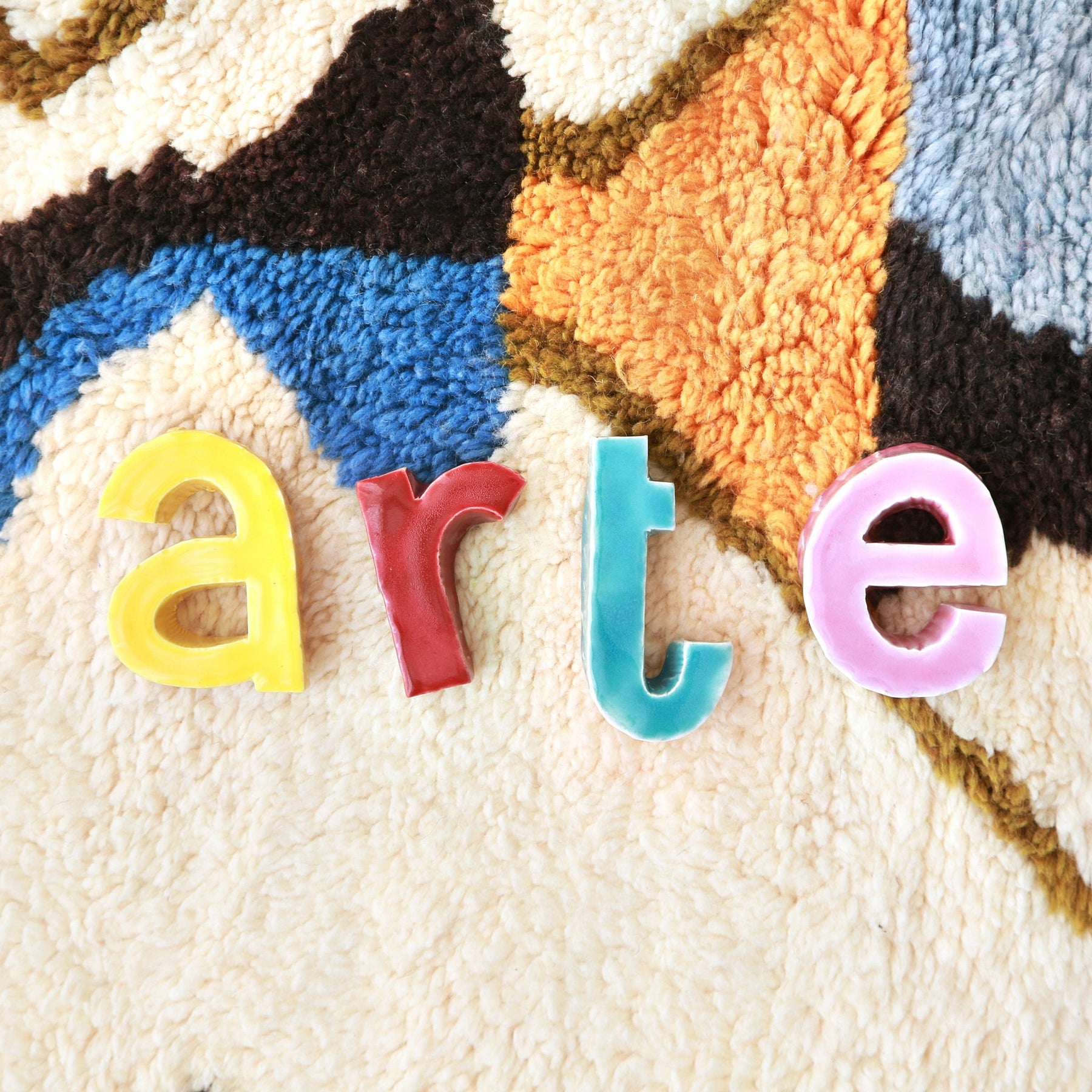 dettaglio ravvicinato di un tappeto beni mrirt con disegni astratti color pastello e lettere colorate in ceramica che formano la parola arte