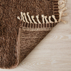 angolo capovolto di un tappeto beni mrirt per evidenziare i nodi della lana e il bordo del tappeto realizzato con linee verticali di marrone chiaro e scuro che si alternano