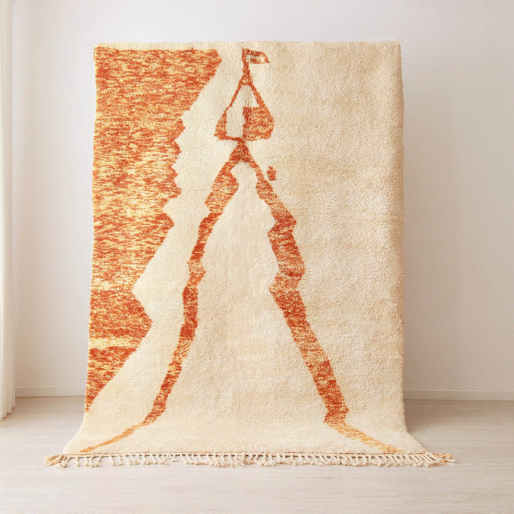 Tappeto beni mrirt tessuto a mano con una base di colore bianco e un raffigurazione stilizzata arancione di un sposa nel suo abito tradizionale . Il tappeto è appeso