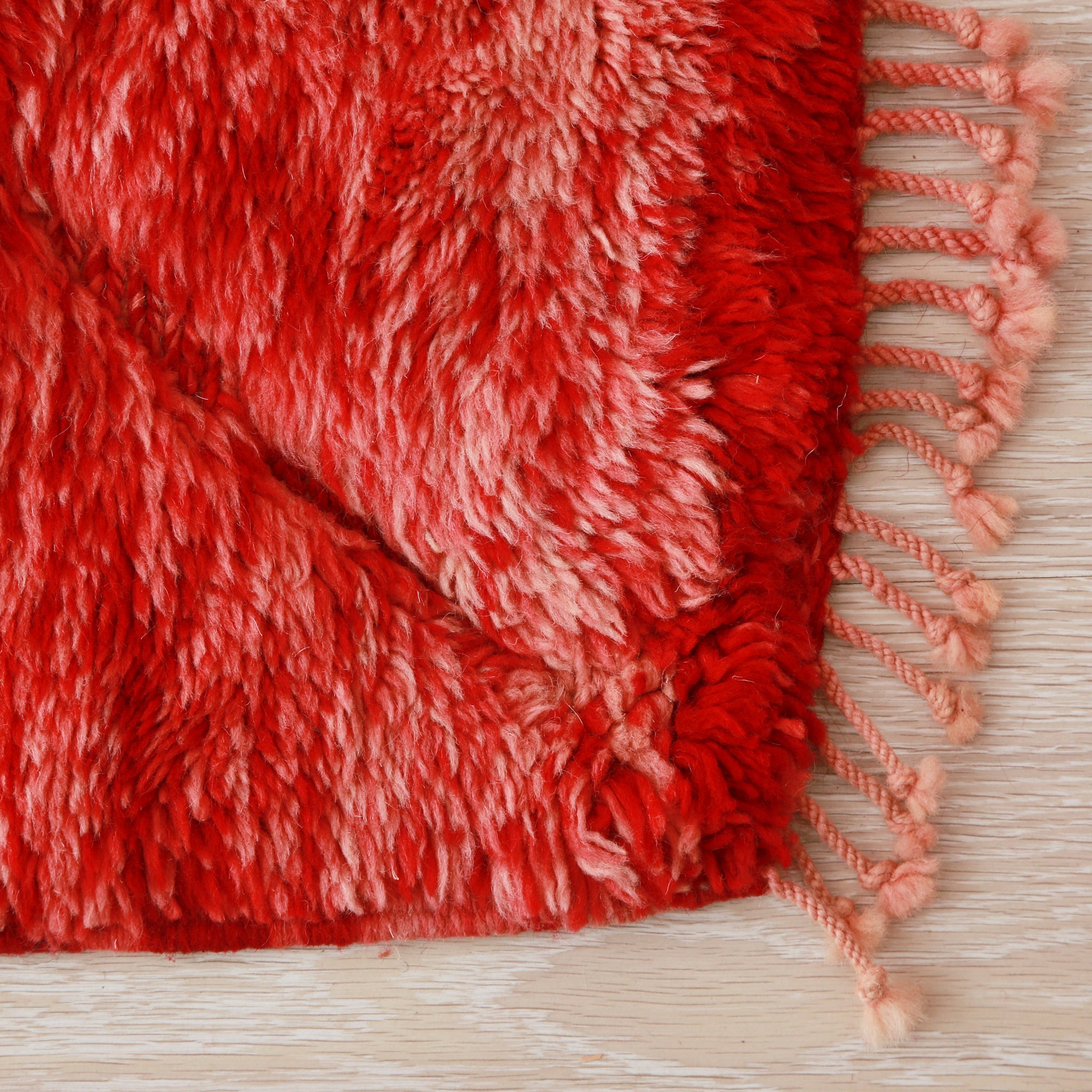 angolo di un tappeto beni mrirt rosso che mette in risalto la lana con diverse sfumature e la corta frangia di un rosso leggero