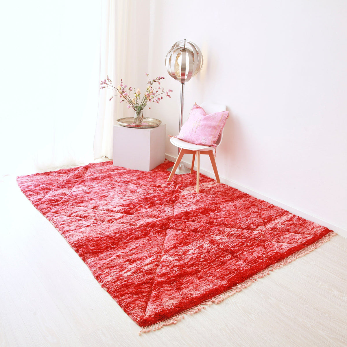 tappeto beni mrirt realizzato a mano con lana rossa disteso sul pavimento.sul tappeto sono presenti una lampanda stile anni 70, una composizione floreale e una sedia con un cuscino rosa in sabra