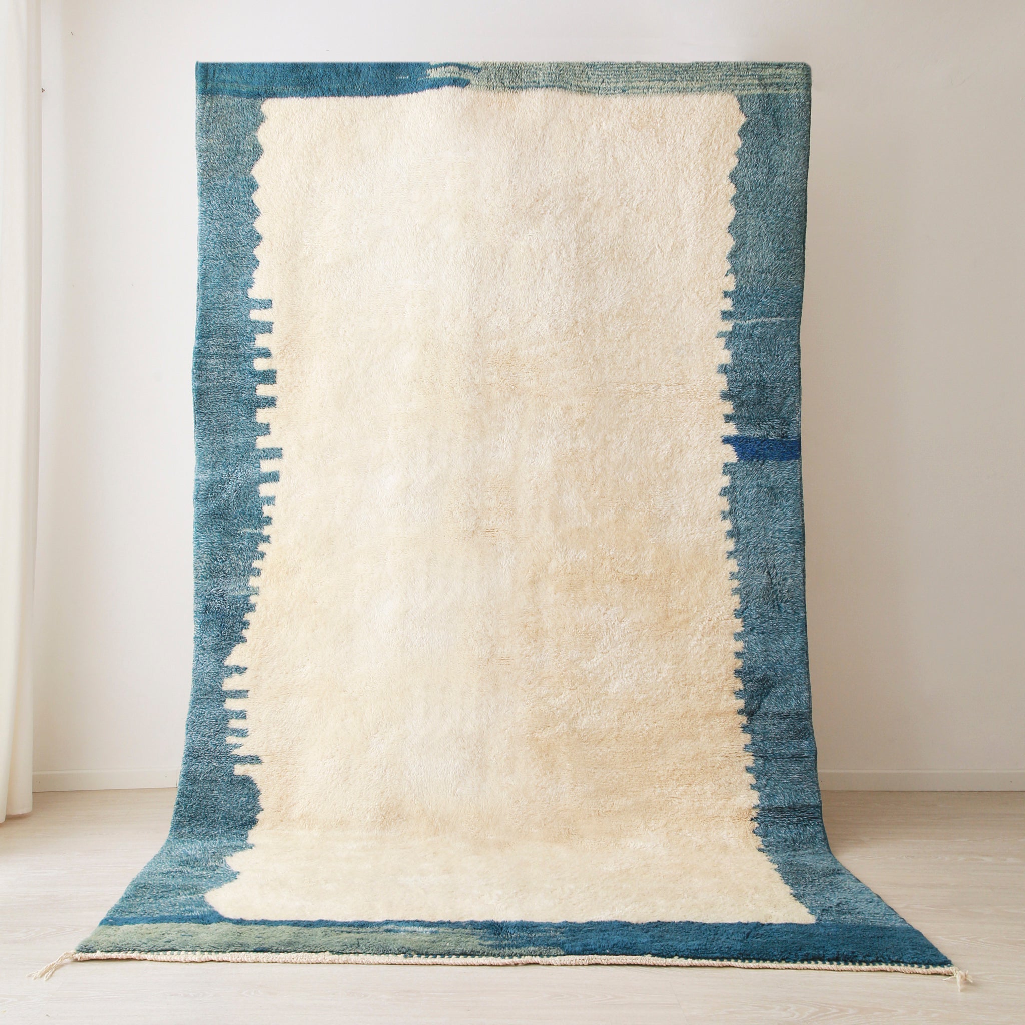 grande tappeto beni mrirt realizzato in lana bianca con un bordi di varie sfumature di blu. La tessitura del bordo ricorda uno skyline di una città