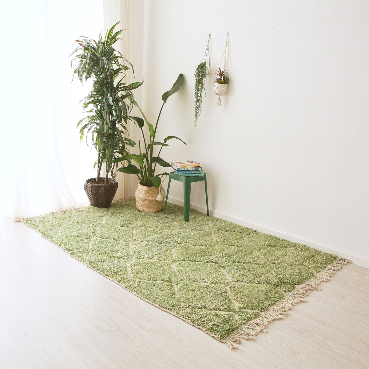Tappeto beni mrirt in lana tinta di verde disteso sul pavimento. Sul tappeto ci  sono due piante e un sgabello in metallo con sopra dei libri