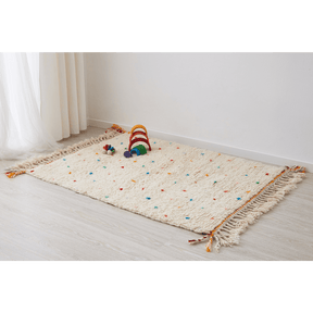 Tappeto beni ourain per cameretta con pois di diversi colori e frange di due colori su base di morbida lana bianca disteso sul pavimento