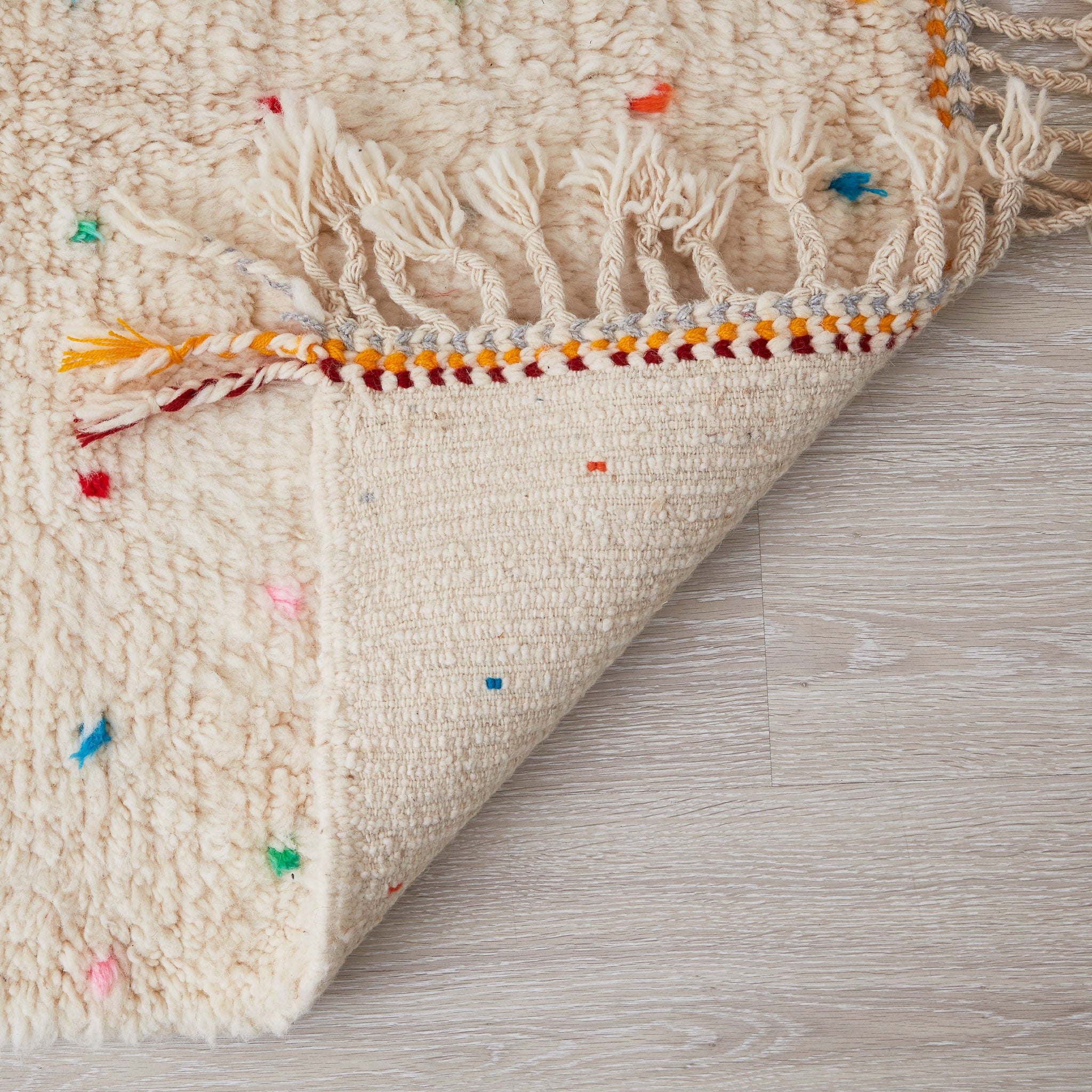 Tappeto beni ourain per cameretta con pois di diversi colori e frange di due colori su base bianca dettaglio del retro