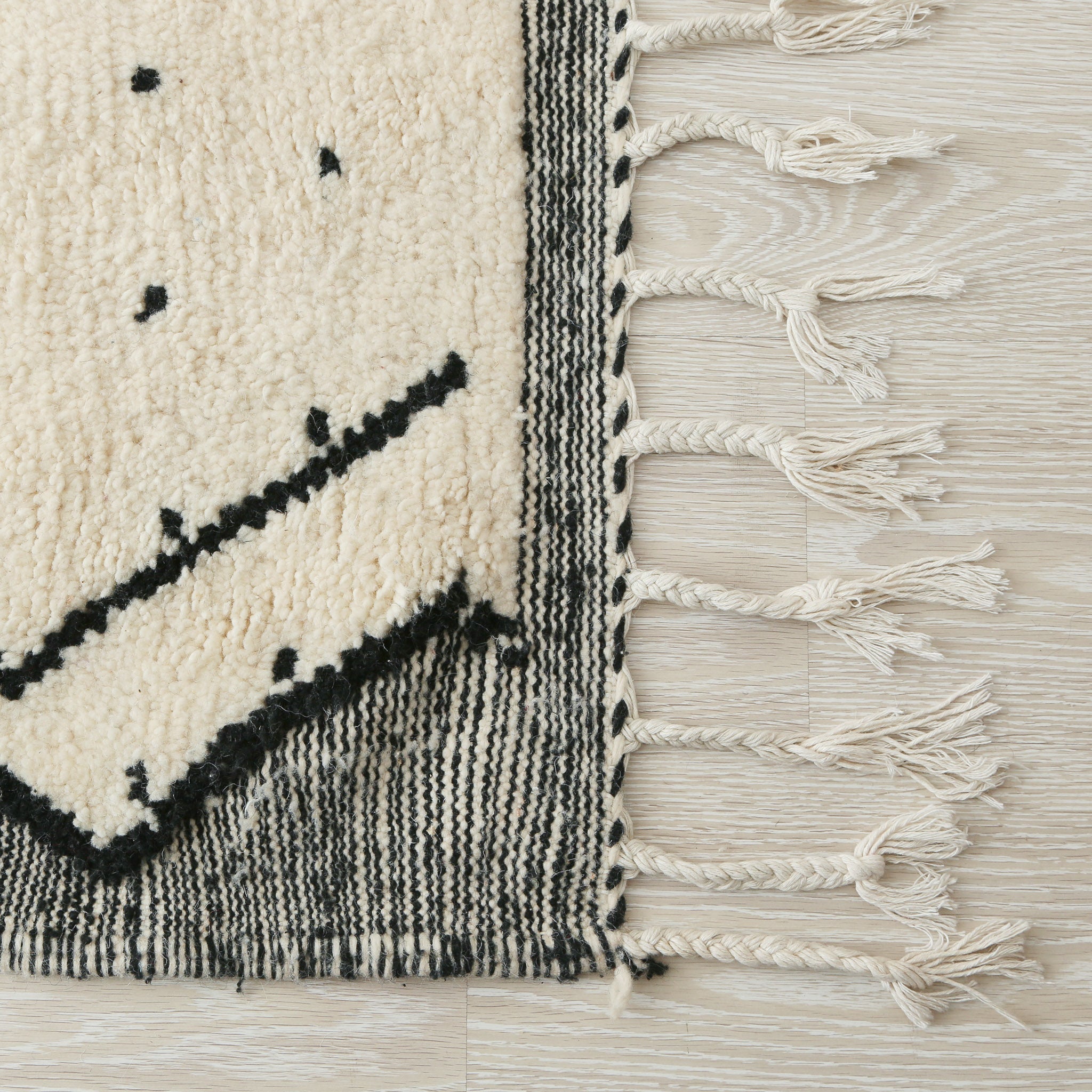 tappeto beni ourain con disegni geometrici a rombi e pois neri  e lati scuri dettaglio della frangia e delle doppia tessitura