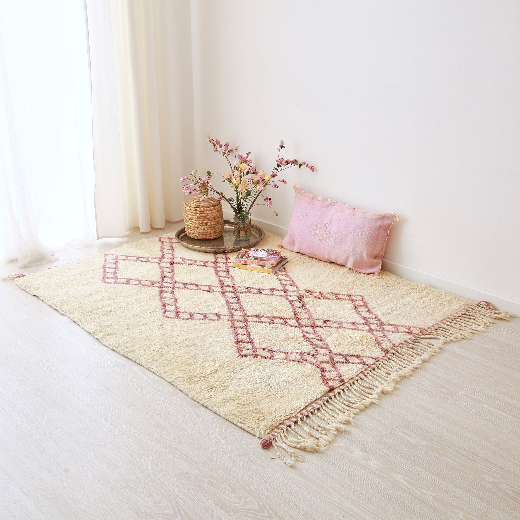 tappeto beni mrirt bianco con rombi lilla che creano quattro catene  che si intracciano disteso sul pavimento. Un lungo tappeto in sabra rosa e una composizione floreale sono appoggiati sul tappeto