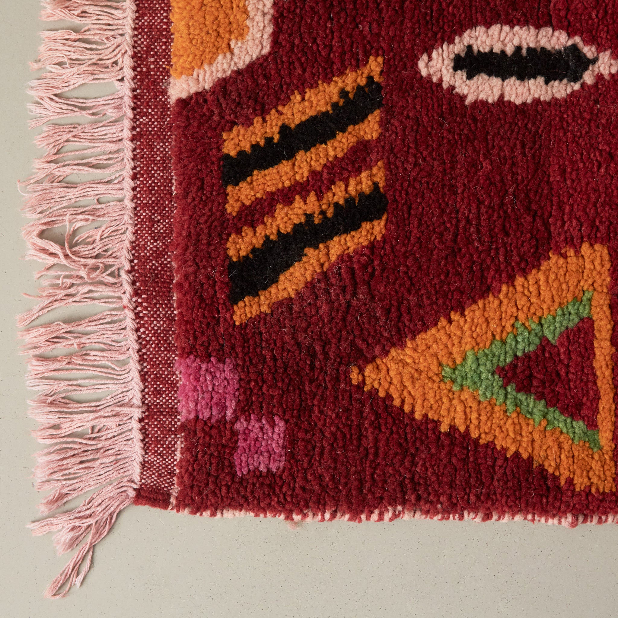 dettaglio della frangia e del pelo corto in lana rossa di un tappeto bouajaad con simboli tradizionali gialli neri verdi