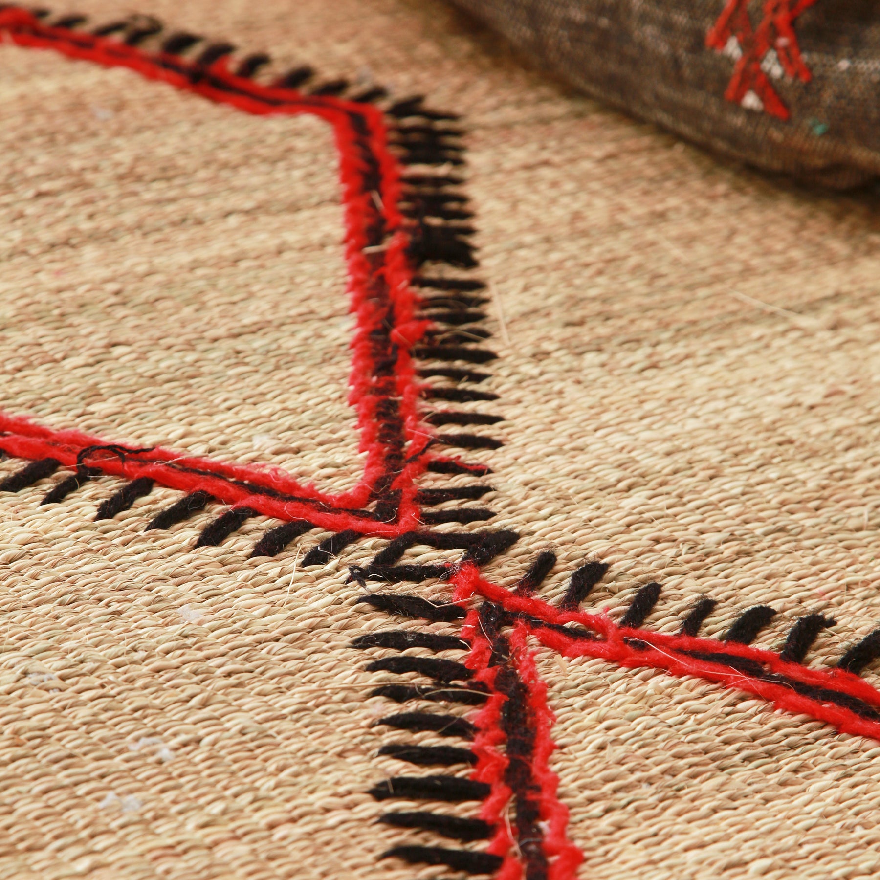 dettaglio di una stuoia hassira in paglia piccola con ricami geometrici in lana neri rossi