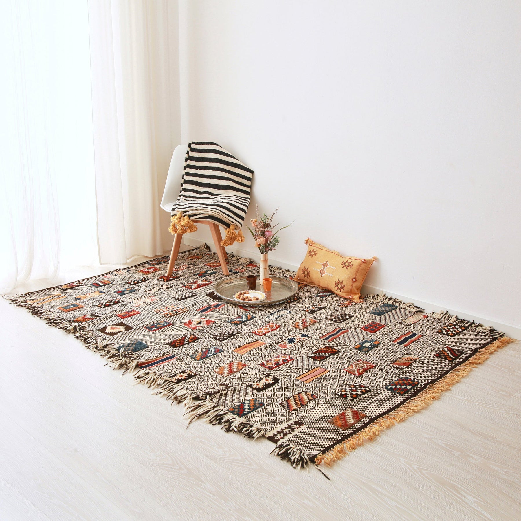tappeto zanafi glaouoi a tessitura piatta con tre differenti tecniche di tessitura posizionato sul pavimento con una sedia un cuscino e piatto e diversi accessori